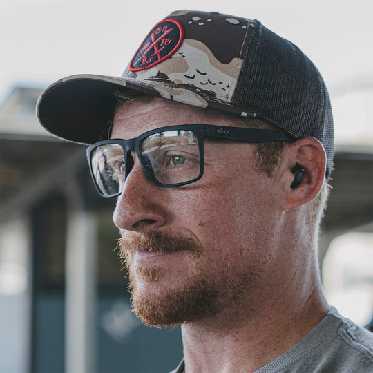 Man wearing a hat and clear glasses in an outdoor setting.