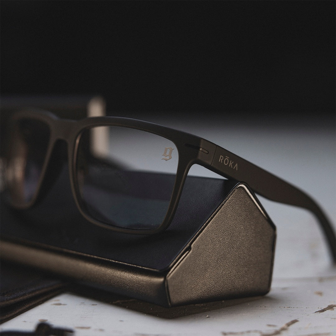 Black glasses with clear lens that have GBRS Group and Roka branding, resting on the black eyeglasses case they come with.