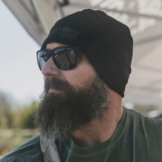 Man wearing a black beanie and sunglasses in an outdoor setting.